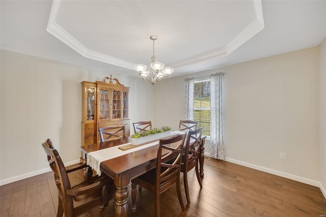 dining space with a raised ceiling, ornamental molding, and dark wood-type flooring