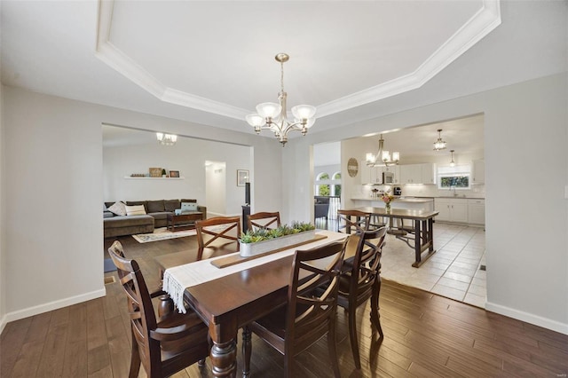 dining room with sink, a tray ceiling, crown molding, an inviting chandelier, and light hardwood / wood-style flooring