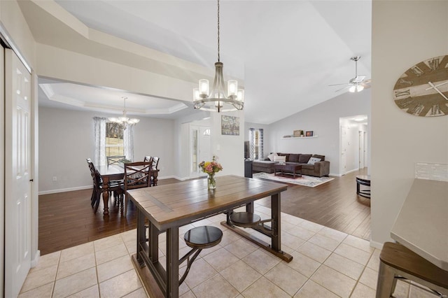 tiled dining space with a raised ceiling, lofted ceiling, and ceiling fan with notable chandelier