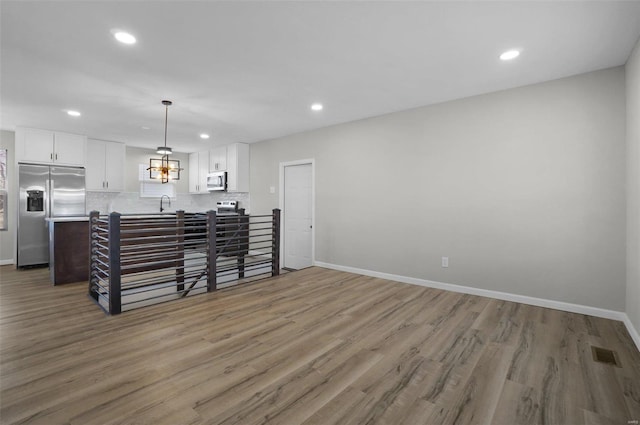 kitchen featuring appliances with stainless steel finishes, wood-type flooring, white cabinets, decorative backsplash, and hanging light fixtures