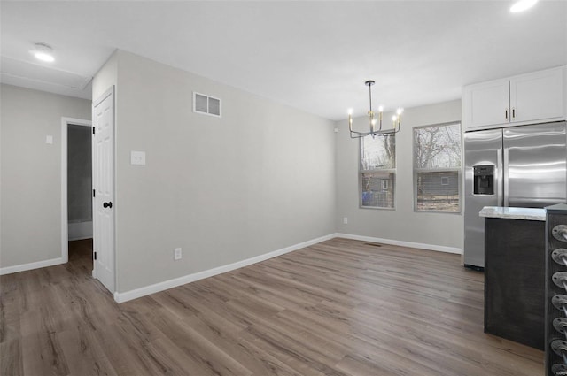 kitchen with white cabinets, hardwood / wood-style flooring, a notable chandelier, stainless steel refrigerator with ice dispenser, and light stone countertops