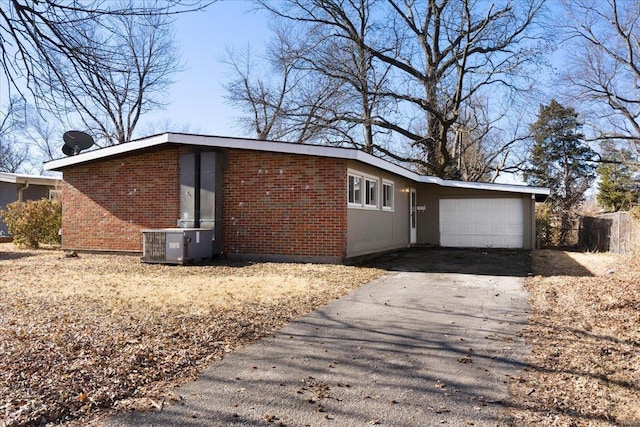 view of property exterior featuring brick siding, cooling unit, aphalt driveway, and a garage