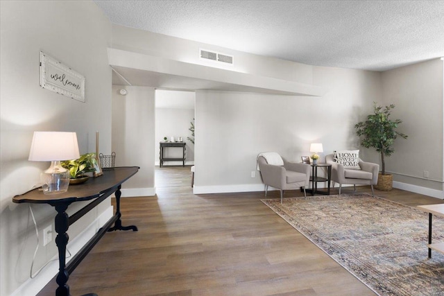 sitting room with baseboards, wood finished floors, visible vents, and a textured ceiling