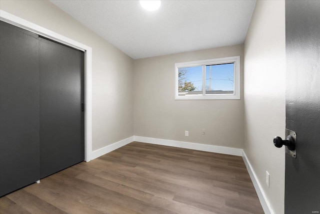 unfurnished bedroom featuring wood finished floors, baseboards, and a closet