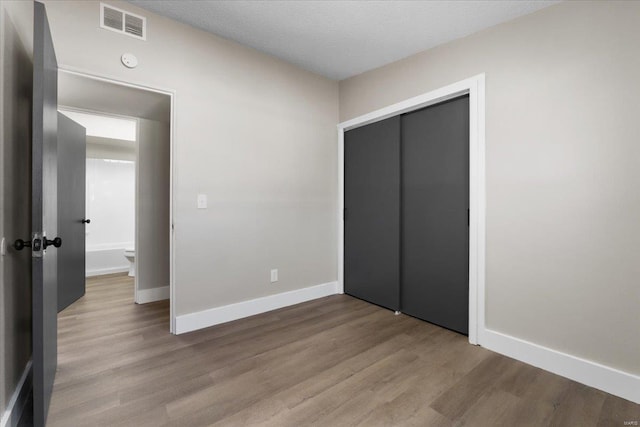 unfurnished bedroom featuring wood finished floors, visible vents, a closet, and baseboards