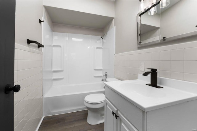 bathroom featuring vanity, wood finished floors, shower / bathing tub combination, tile walls, and toilet