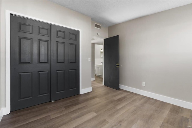 unfurnished bedroom featuring visible vents, baseboards, a closet, and wood finished floors