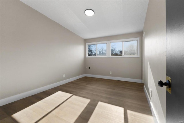 spare room featuring baseboards, lofted ceiling, and wood finished floors