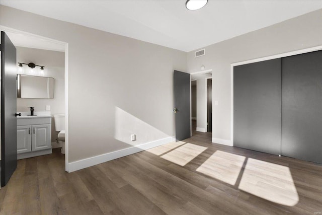 unfurnished bedroom featuring wood finished floors, baseboards, visible vents, a sink, and a closet