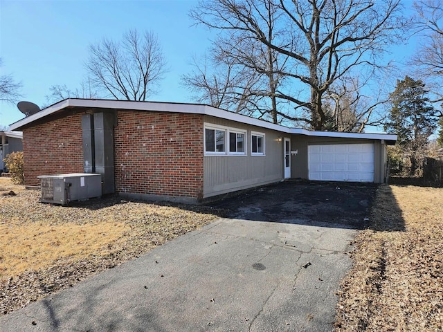 view of front facade featuring central air condition unit, brick siding, an attached garage, and driveway