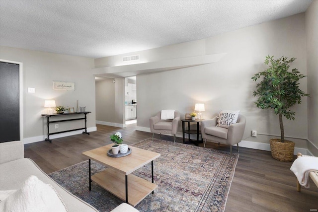 living room with baseboards, wood finished floors, visible vents, and a textured ceiling