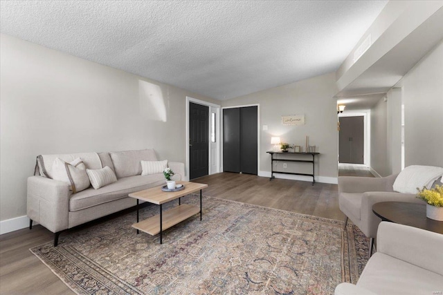 living area featuring lofted ceiling, wood finished floors, baseboards, and a textured ceiling