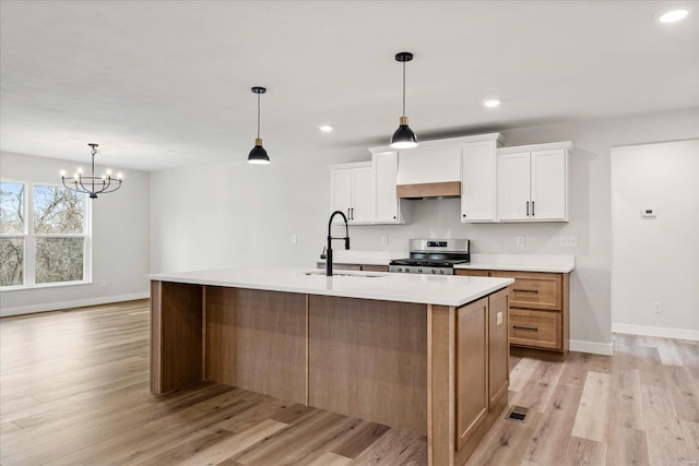 kitchen with light countertops, white cabinets, a large island with sink, and stainless steel stove