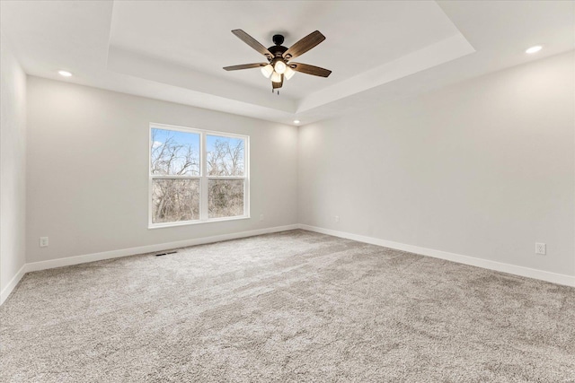 unfurnished room featuring carpet, a raised ceiling, ceiling fan, and baseboards