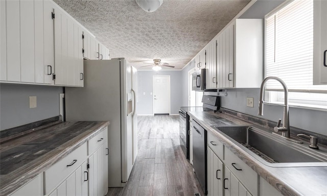 kitchen with a ceiling fan, appliances with stainless steel finishes, wood finished floors, a textured ceiling, and a sink