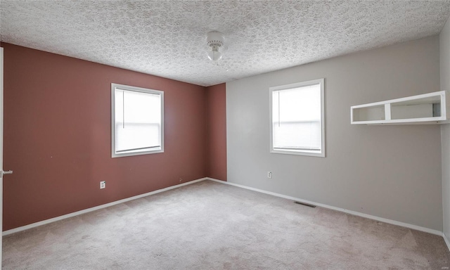 spare room with carpet, a textured ceiling, visible vents, and baseboards