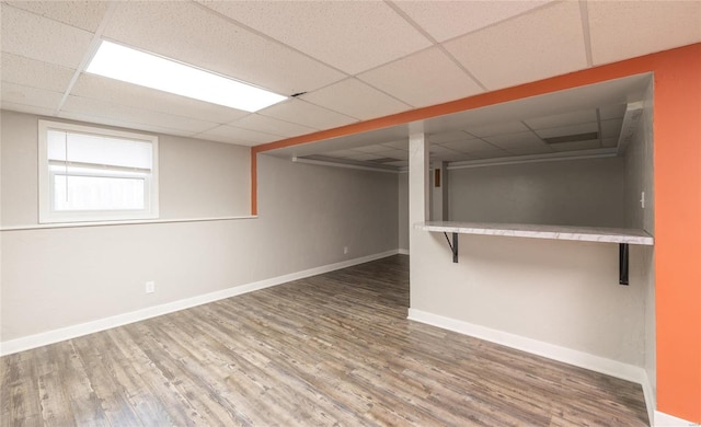 basement featuring wood finished floors, a paneled ceiling, and baseboards