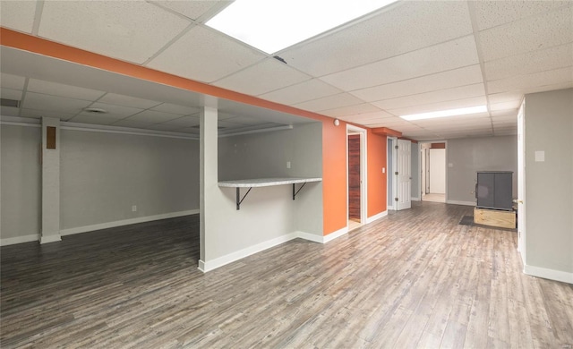 finished below grade area with a drop ceiling, baseboards, and wood finished floors