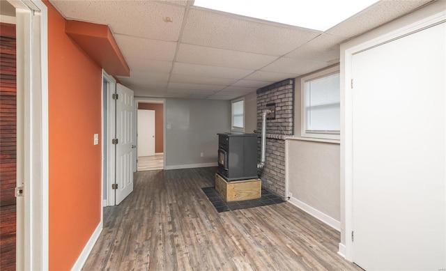 unfurnished living room with a drop ceiling, wood finished floors, a wood stove, and baseboards