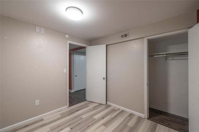 unfurnished bedroom featuring baseboards, a closet, visible vents, and light wood-style floors