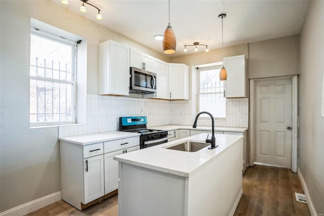 kitchen featuring pendant lighting, sink, white cabinetry, a center island with sink, and black range oven