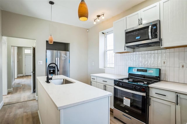 kitchen with sink, a kitchen island with sink, stainless steel appliances, white cabinets, and decorative backsplash