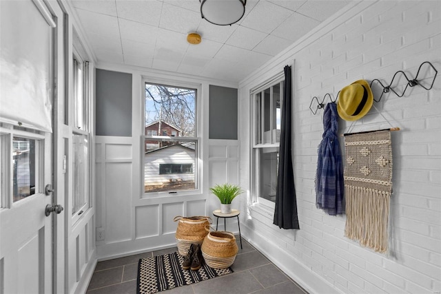 mudroom with crown molding, brick wall, and dark tile patterned flooring