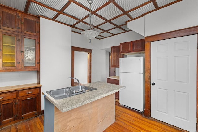 kitchen with a sink, light countertops, freestanding refrigerator, wood-type flooring, and glass insert cabinets