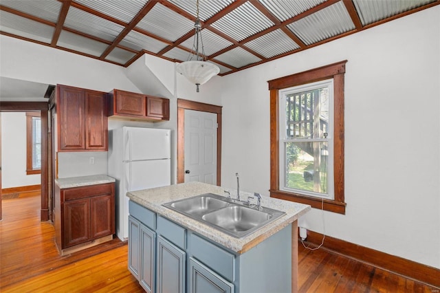 kitchen featuring a sink, baseboards, light countertops, freestanding refrigerator, and light wood-style floors