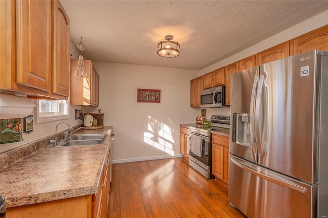 kitchen featuring appliances with stainless steel finishes, sink, a textured ceiling, and light hardwood / wood-style floors