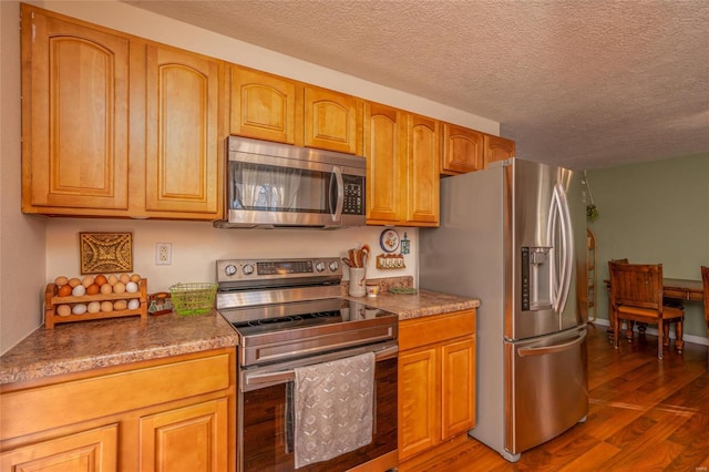 kitchen with dark wood-type flooring, a textured ceiling, and appliances with stainless steel finishes