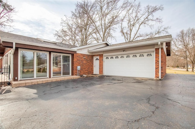 ranch-style house featuring a garage, roof with shingles, aphalt driveway, and brick siding