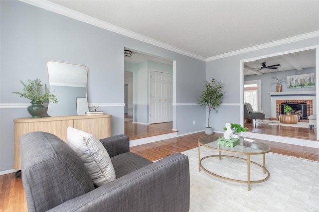 living area featuring crown molding, a fireplace, a ceiling fan, wood finished floors, and baseboards