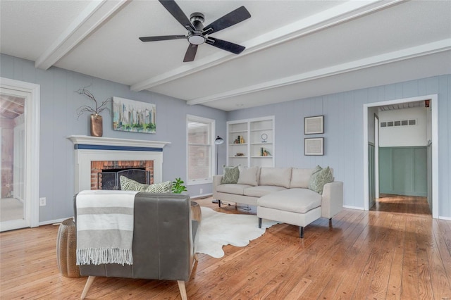 living room with a brick fireplace, beam ceiling, visible vents, and hardwood / wood-style flooring