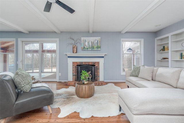 living area with a wealth of natural light, beam ceiling, a fireplace, and wood finished floors