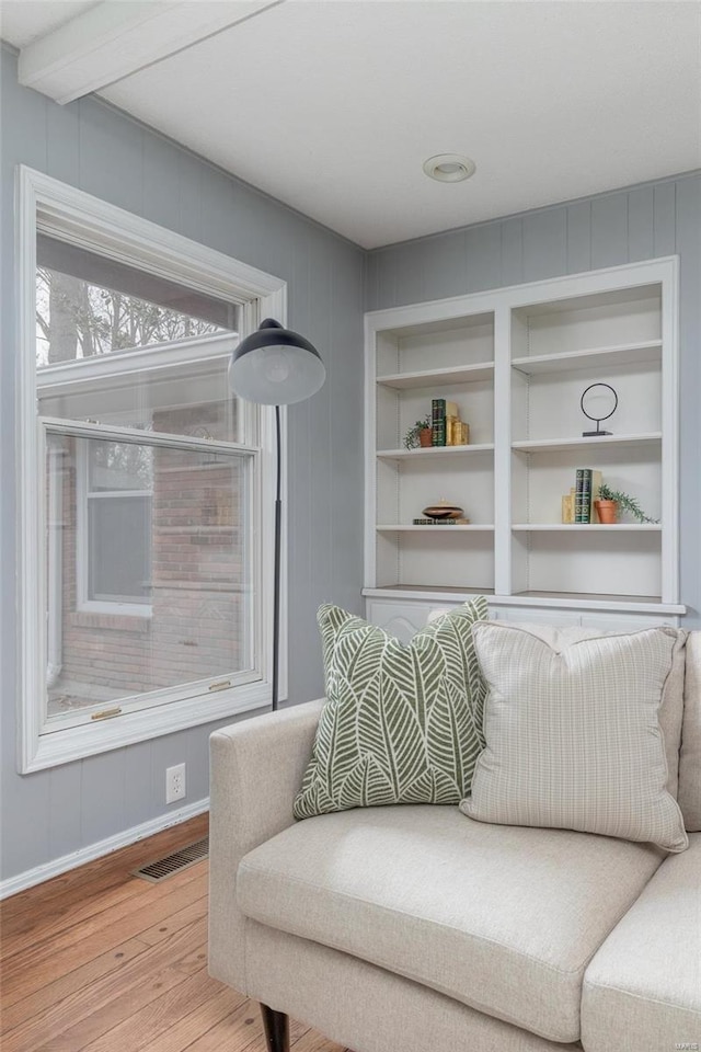 sitting room featuring baseboards, visible vents, built in features, beamed ceiling, and light wood-style floors