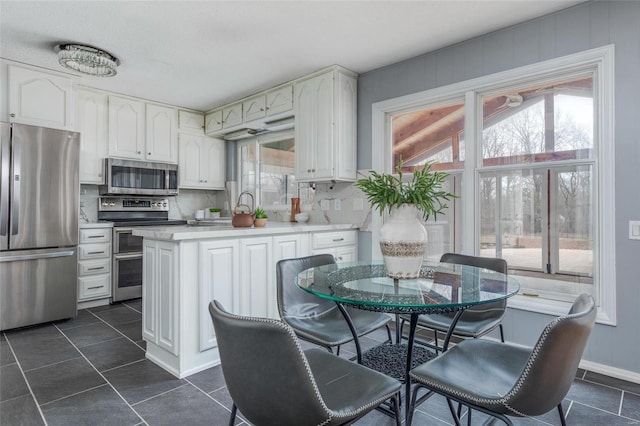 kitchen with light countertops, appliances with stainless steel finishes, a peninsula, and backsplash