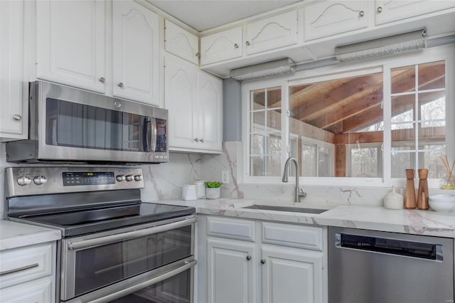 kitchen featuring tasteful backsplash, appliances with stainless steel finishes, white cabinetry, a sink, and light stone countertops