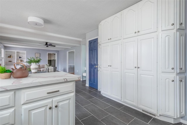 kitchen with a textured ceiling, ceiling fan, visible vents, white cabinetry, and light stone countertops