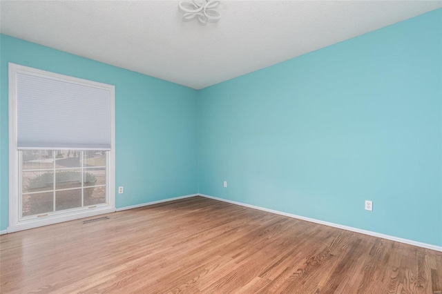 spare room featuring baseboards, visible vents, and wood finished floors