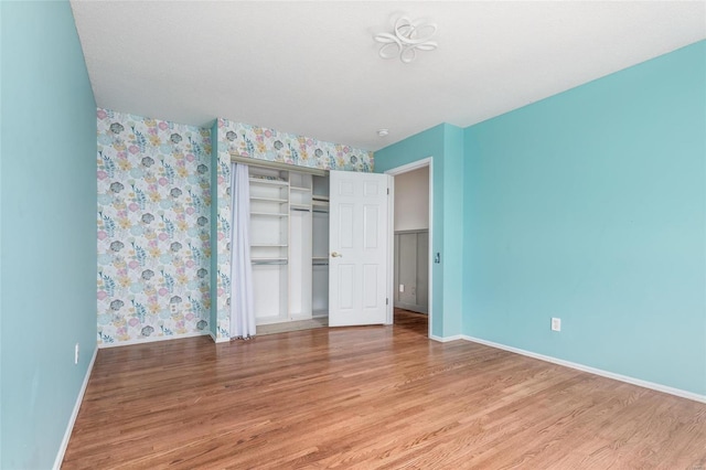 unfurnished bedroom with baseboards, a closet, wood finished floors, and wallpapered walls