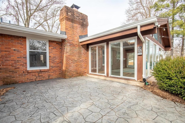 rear view of house featuring a patio area, brick siding, and a chimney