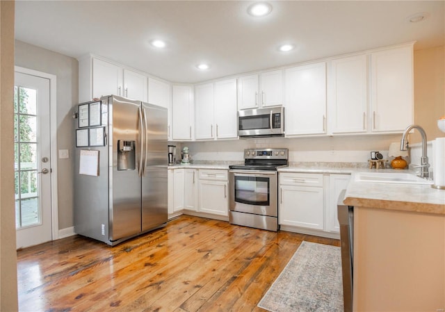 kitchen with stainless steel appliances, white cabinetry, sink, and light wood-type flooring