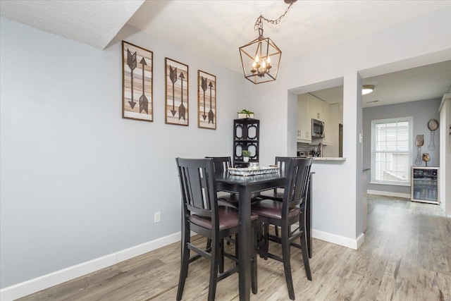 dining room with an inviting chandelier, wine cooler, and light wood-type flooring