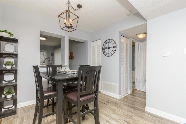 dining area with light hardwood / wood-style floors, a textured ceiling, and a notable chandelier