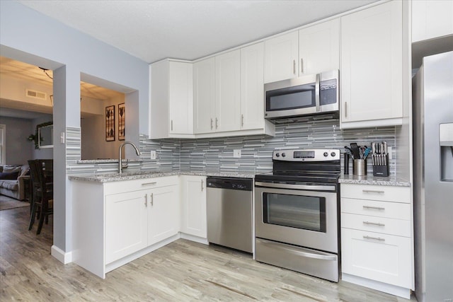 kitchen featuring light stone countertops, decorative backsplash, stainless steel appliances, and white cabinets