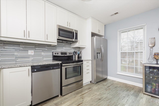 kitchen with white cabinetry, appliances with stainless steel finishes, light stone counters, and decorative backsplash