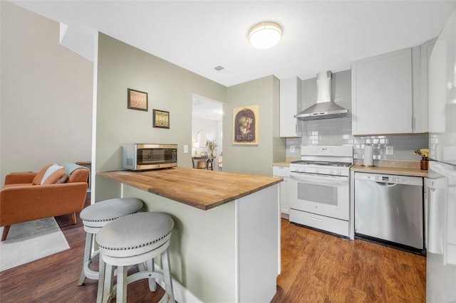 kitchen with appliances with stainless steel finishes, wood counters, white cabinets, a kitchen breakfast bar, and wall chimney exhaust hood