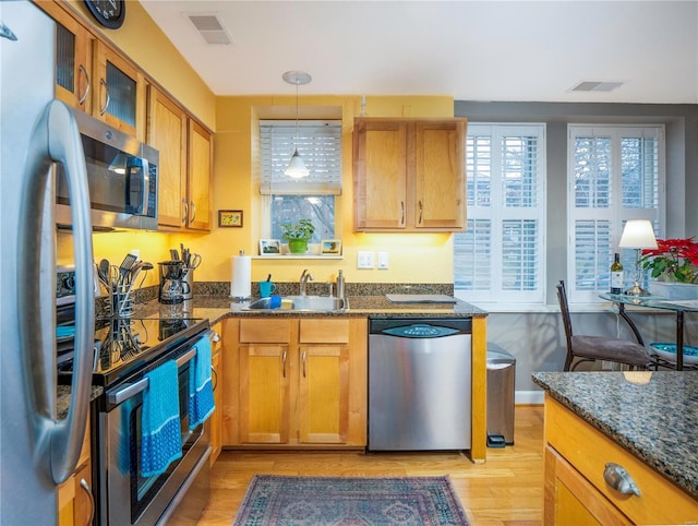 kitchen with sink, light hardwood / wood-style flooring, stainless steel appliances, decorative light fixtures, and dark stone counters