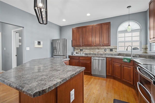 kitchen featuring sink, light wood-type flooring, appliances with stainless steel finishes, a kitchen island, and pendant lighting